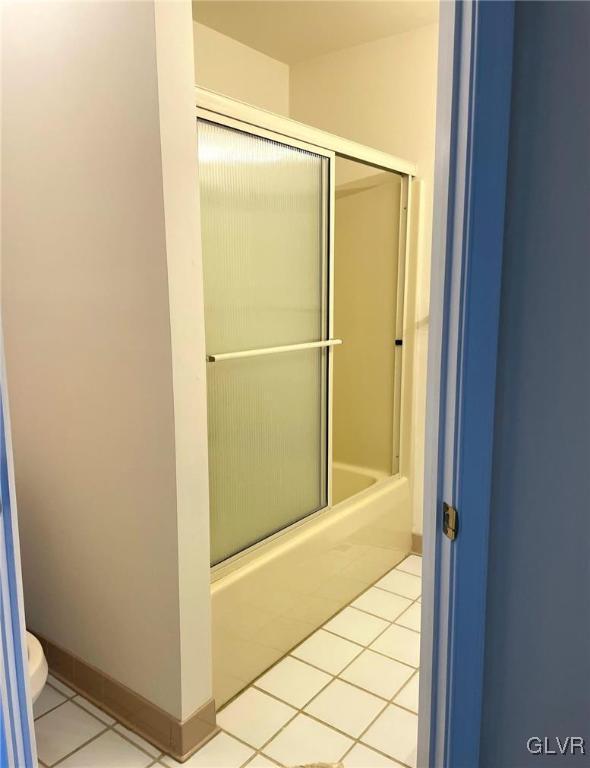 bathroom featuring tile patterned floors, baseboards, toilet, and shower / bath combination with glass door