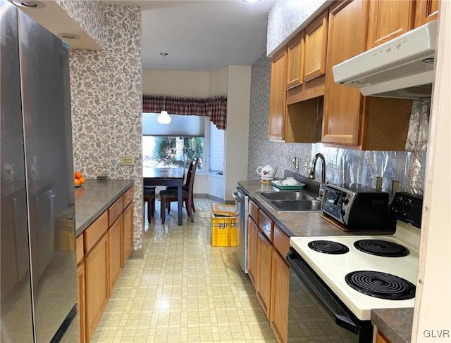 kitchen with under cabinet range hood, dark countertops, appliances with stainless steel finishes, and a sink