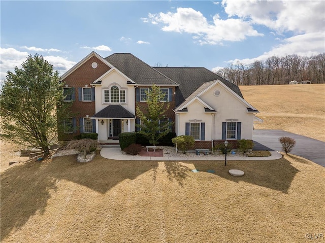 view of front facade featuring stucco siding, brick siding, and driveway