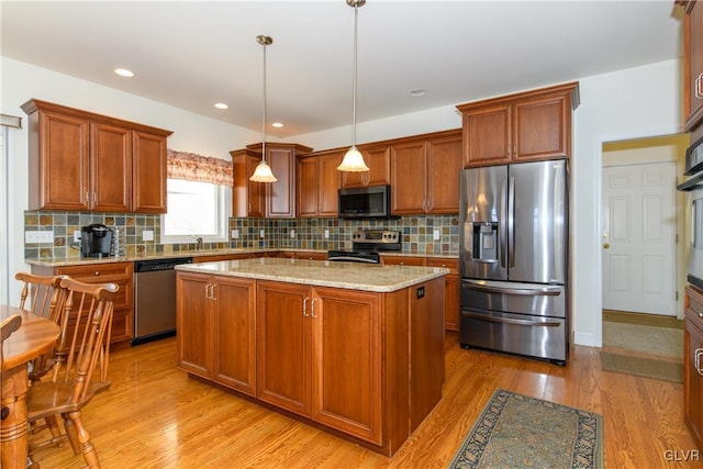 kitchen with a kitchen island, light stone counters, appliances with stainless steel finishes, light wood-style floors, and hanging light fixtures