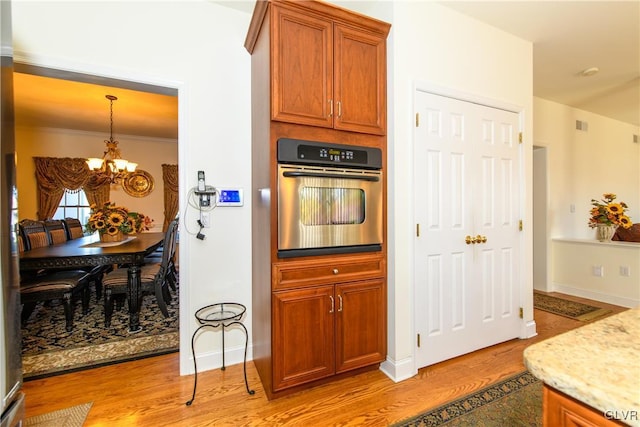 kitchen with brown cabinetry, baseboards, light wood finished floors, stainless steel oven, and a notable chandelier