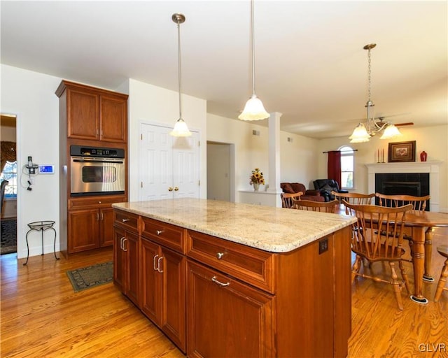 kitchen featuring pendant lighting, light stone countertops, light wood-type flooring, and stainless steel oven