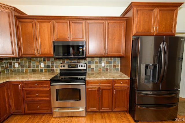 kitchen featuring light wood-type flooring, light stone counters, tasteful backsplash, appliances with stainless steel finishes, and brown cabinetry