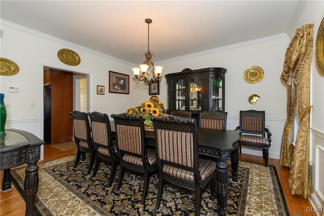 dining room with a wainscoted wall, a notable chandelier, wood finished floors, and crown molding