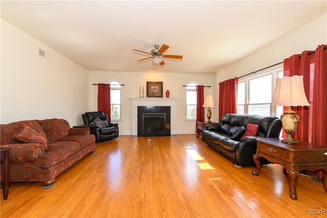 living room with ceiling fan, visible vents, light wood-style flooring, and a tiled fireplace