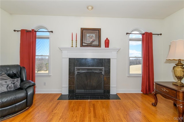 living area with a tile fireplace, baseboards, and wood finished floors