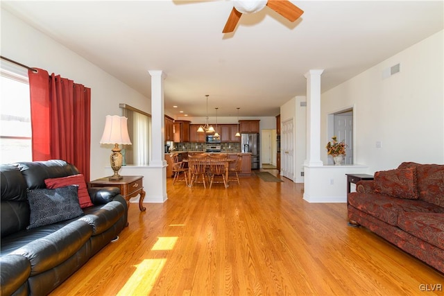 living area featuring plenty of natural light, light wood-style floors, visible vents, and ornate columns