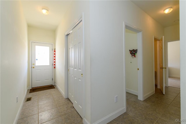 hall with light tile patterned floors, visible vents, and baseboards