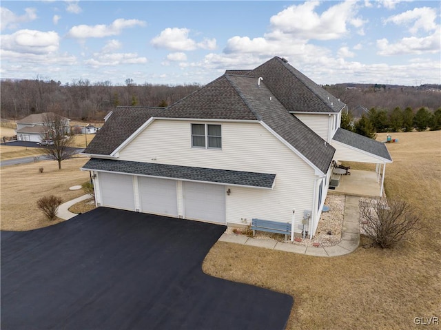 view of side of property with a garage, roof with shingles, and driveway