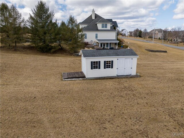 exterior space featuring a storage shed, an outdoor structure, a yard, and roof with shingles