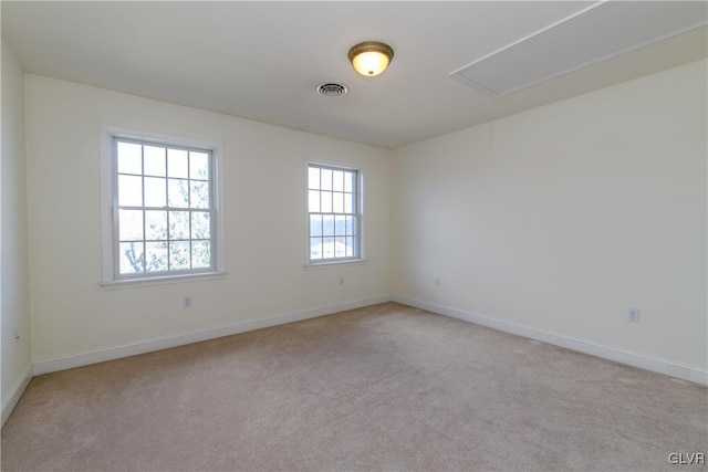 empty room featuring visible vents, baseboards, light colored carpet, and attic access