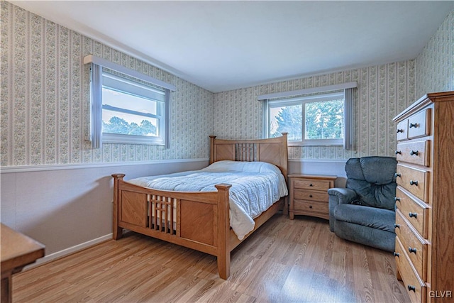 bedroom with a wainscoted wall, light wood-style flooring, and wallpapered walls