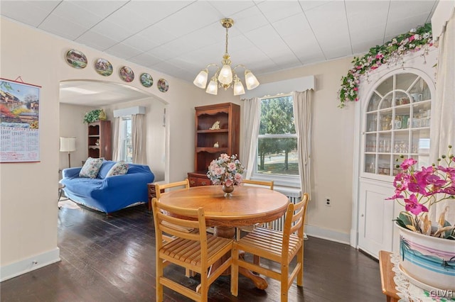 dining room featuring arched walkways, a notable chandelier, baseboards, and dark wood-style floors