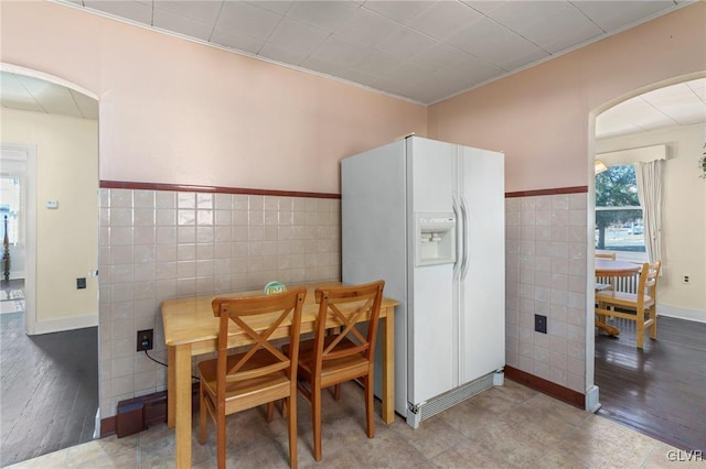 dining space featuring tile walls, wood finished floors, arched walkways, and wainscoting