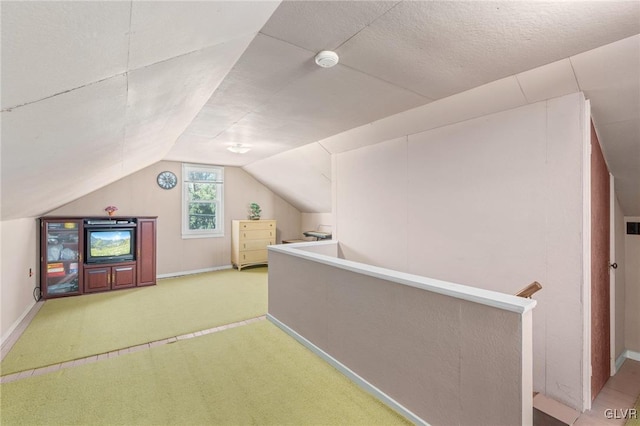 additional living space with a textured ceiling, baseboards, light colored carpet, and vaulted ceiling