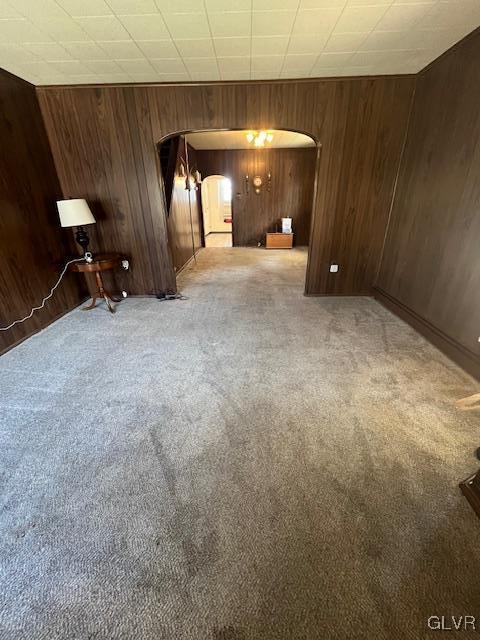 carpeted spare room with arched walkways and wooden walls