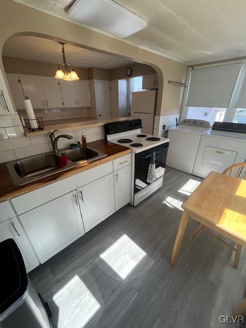 kitchen featuring white appliances, wood finished floors, a sink, white cabinetry, and independent washer and dryer