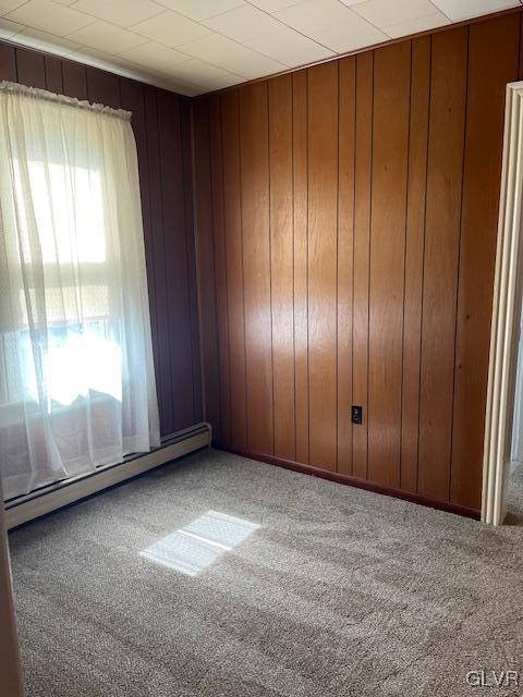 carpeted spare room featuring wooden walls and a baseboard radiator