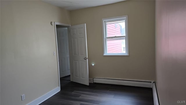 empty room featuring a baseboard radiator, baseboards, and dark wood-type flooring