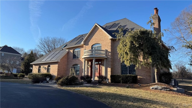 view of front of house with a front lawn, brick siding, solar panels, and a balcony