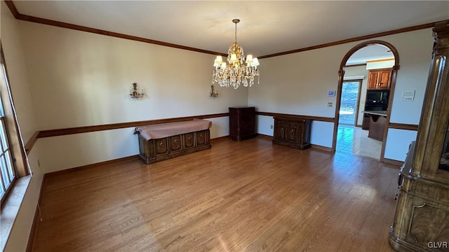 unfurnished dining area with baseboards, light wood-style floors, an inviting chandelier, and crown molding