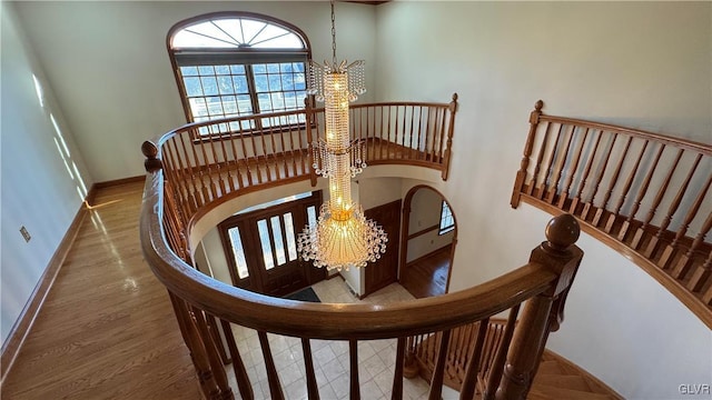 staircase featuring baseboards, a notable chandelier, a high ceiling, and wood finished floors