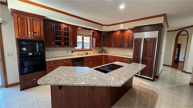 kitchen with backsplash, a center island, glass insert cabinets, light stone counters, and black appliances