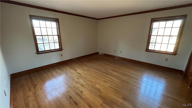 empty room with a wealth of natural light, wood finished floors, and crown molding