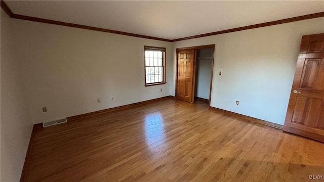 empty room featuring visible vents, baseboards, crown molding, and light wood-style floors