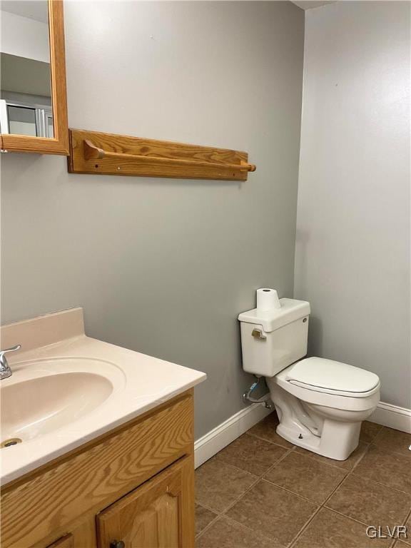 half bathroom with baseboards, toilet, vanity, and tile patterned flooring