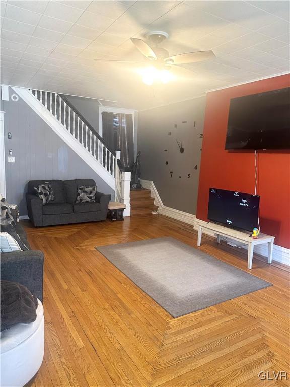 unfurnished living room featuring stairs, parquet floors, a ceiling fan, and baseboards