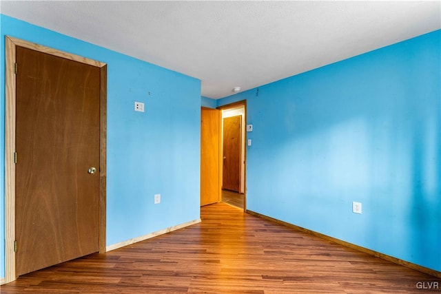 spare room with baseboards and wood finished floors