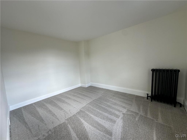 carpeted spare room featuring radiator and baseboards