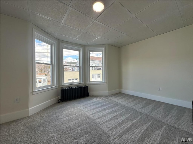 empty room with carpet flooring, radiator, a paneled ceiling, and baseboards