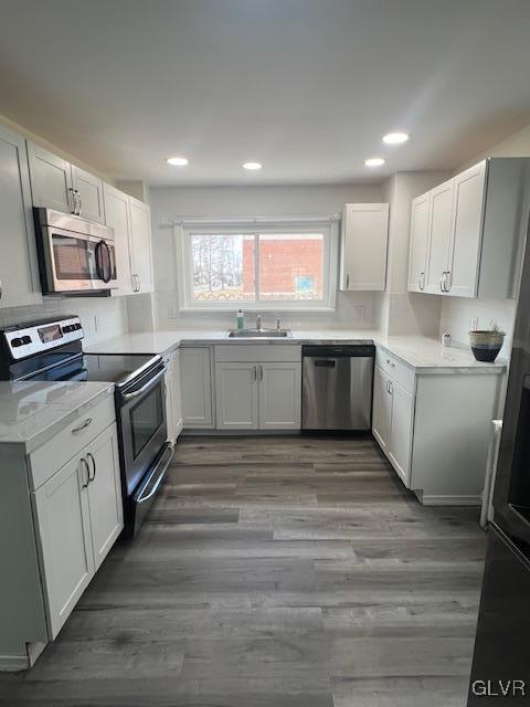 kitchen with appliances with stainless steel finishes, wood finished floors, light countertops, and a sink