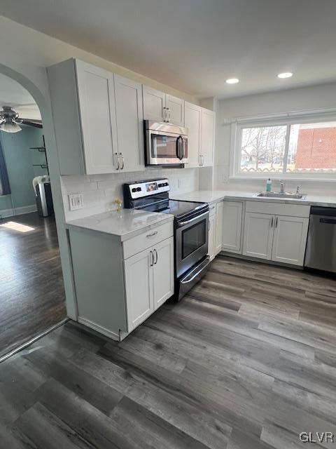 kitchen with arched walkways, stainless steel appliances, light countertops, and dark wood-style flooring