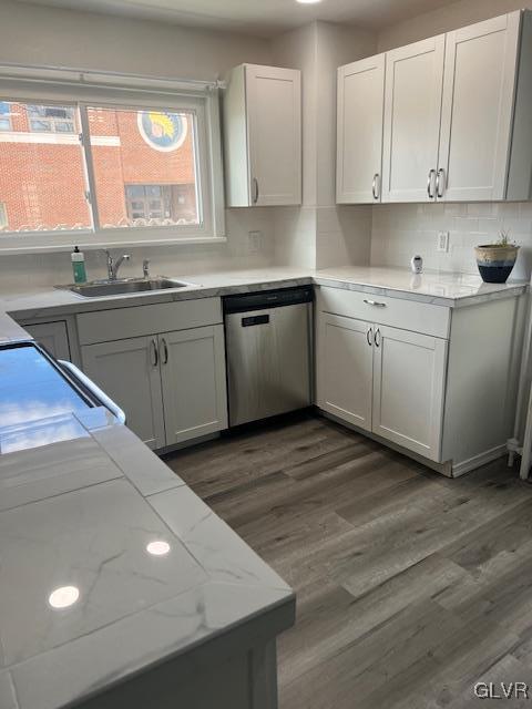 kitchen with a sink, light stone counters, wood finished floors, decorative backsplash, and dishwasher