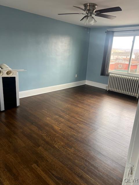 empty room with ceiling fan, radiator heating unit, baseboards, and dark wood-style flooring