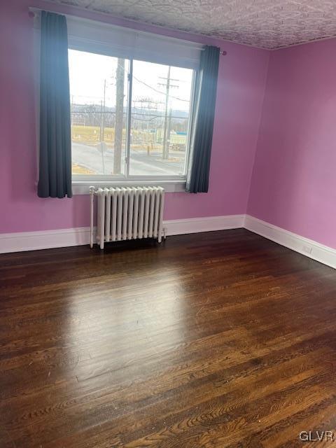 empty room with baseboards, a textured ceiling, dark wood finished floors, and radiator heating unit