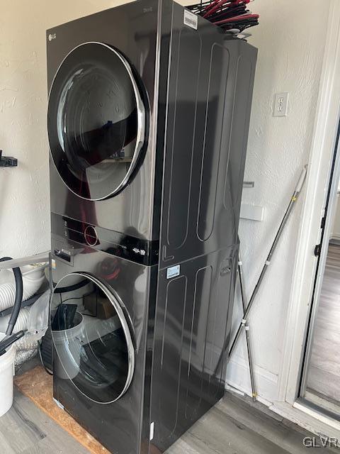 laundry area with stacked washer and clothes dryer, wood finished floors, laundry area, and a textured wall