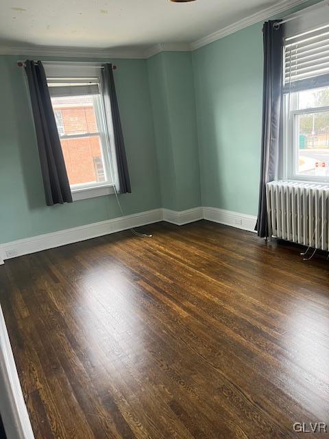 empty room featuring radiator heating unit, dark wood-style floors, a wealth of natural light, and ornamental molding