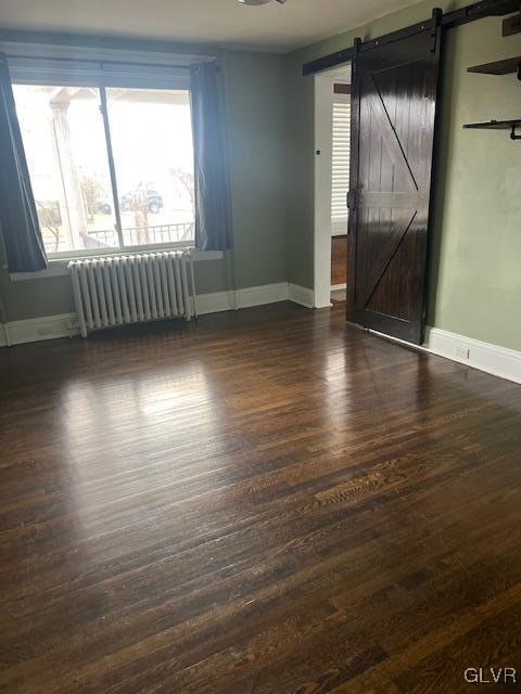 empty room with dark wood-type flooring, baseboards, radiator heating unit, and a barn door