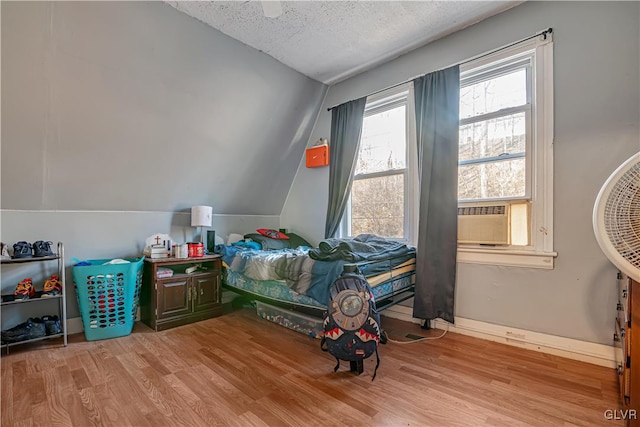 bedroom featuring vaulted ceiling, cooling unit, wood finished floors, and a textured ceiling