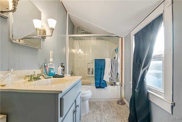 bathroom with toilet, wood finished floors, combined bath / shower with glass door, vanity, and vaulted ceiling