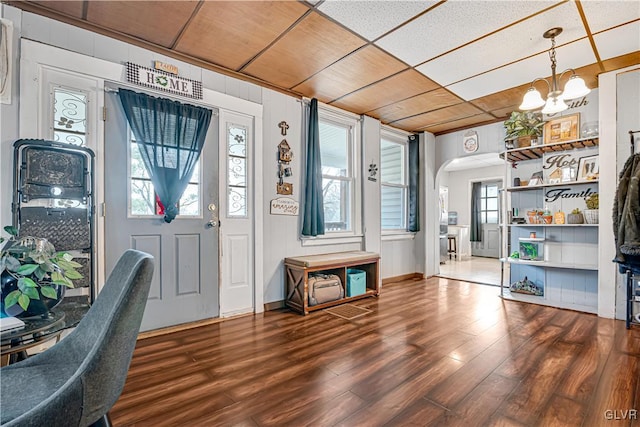 foyer with arched walkways, an inviting chandelier, and wood finished floors