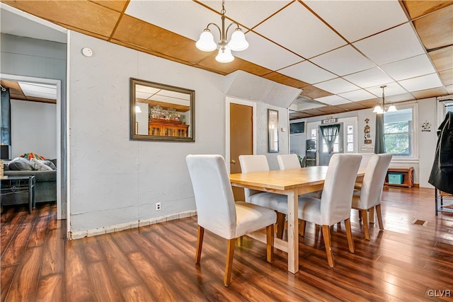 dining space with an inviting chandelier, a paneled ceiling, and dark wood-style flooring