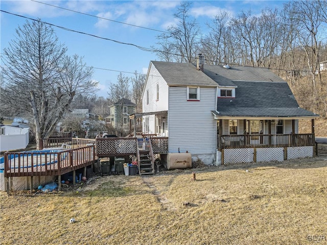 rear view of house featuring a shingled roof, a porch, a wooden deck, a yard, and heating fuel