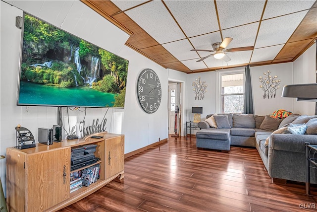 living area featuring a drop ceiling, baseboards, wood finished floors, and a ceiling fan