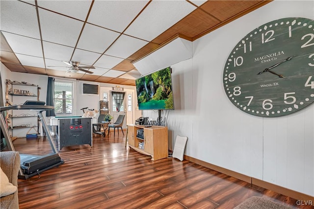 workout room featuring a ceiling fan, wood finished floors, baseboards, and a paneled ceiling