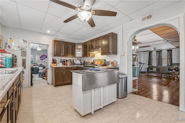 kitchen with visible vents, ceiling fan, under cabinet range hood, a drop ceiling, and arched walkways